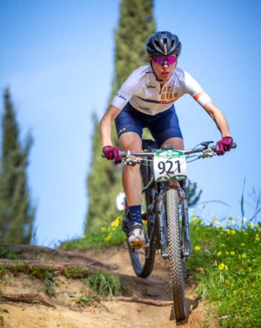 Ana Gay coming down a steep dirt drop on her mountain bike, front wheel in the air