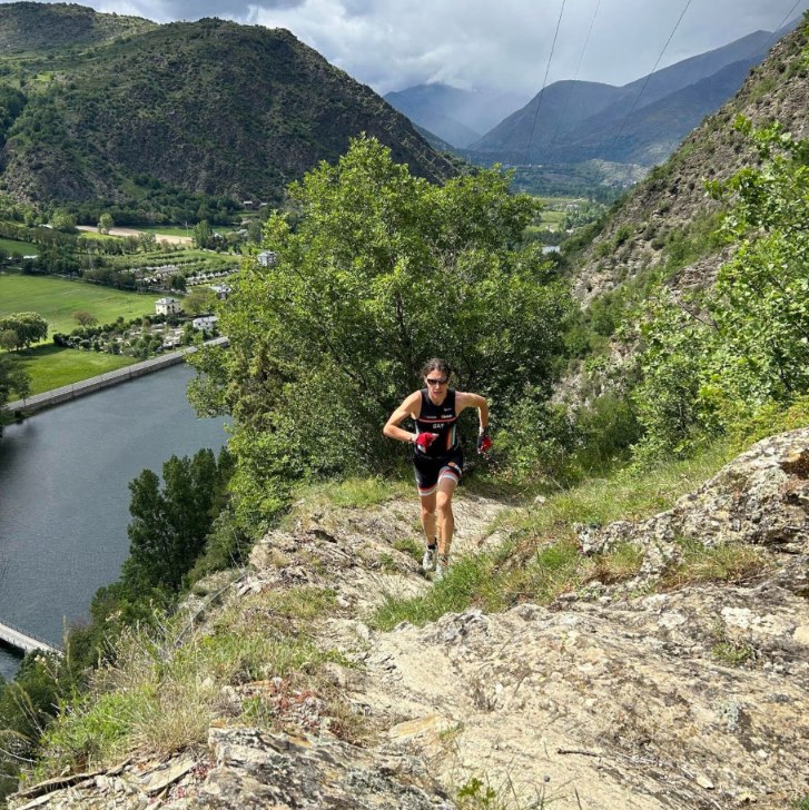 Ana Gay running up a rocky ridge high above a river and a green valley